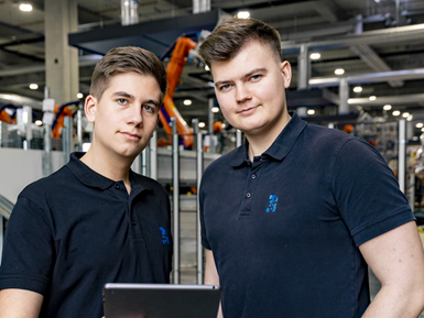 Zwei Auszubildende der EBZ Gruppe sind vor Industrierobotern abgebildet. Ausbildung 4.0 – Digitalisierung wird in der Ausbildung bei EBZ groß geschrieben. 