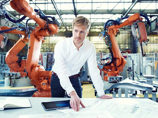 An employee is working with a layout in front of an industrial robot system.