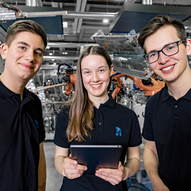 Three EBZ Group trainees in front of industrial robots. Training 4.0 - Digitization is a top priority in the vocational training at the EBZ Group.