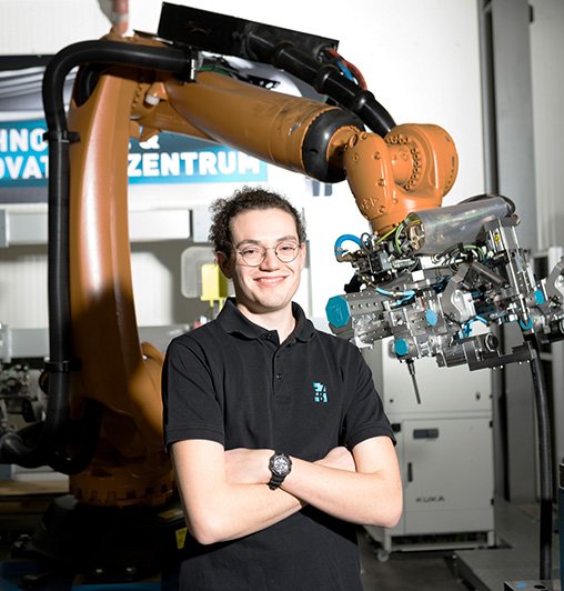 Ein dualer Student im Bereich Mechatronik steht vor einem Industrieroboter.